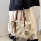 Rounded beige woven straw beach handbag with an adjustable strap
