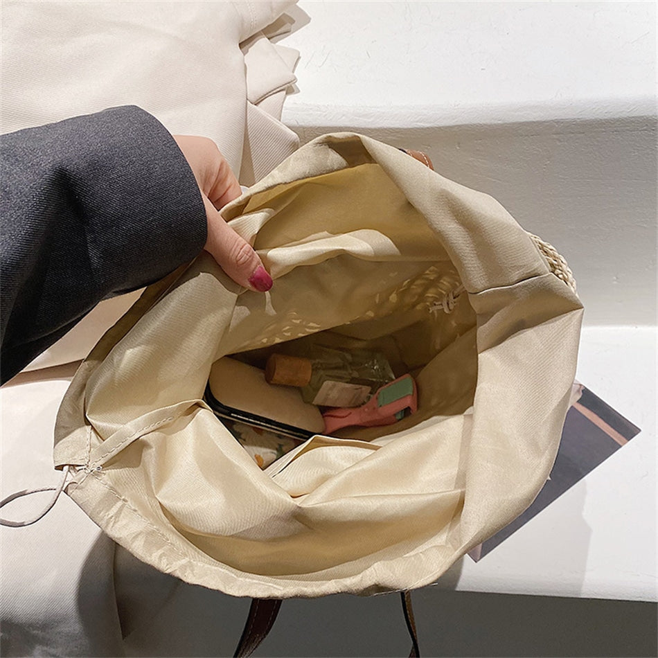 Rounded beige woven straw beach handbag with an adjustable strap