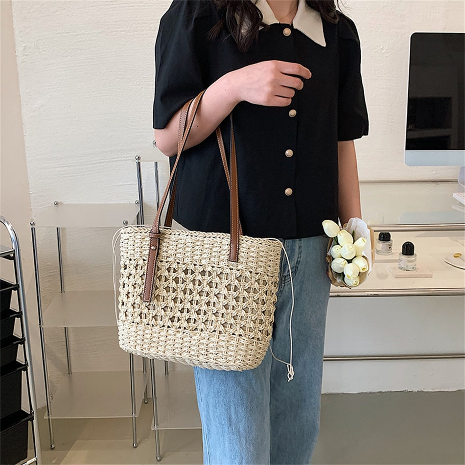 Rounded beige woven straw beach handbag with an adjustable strap