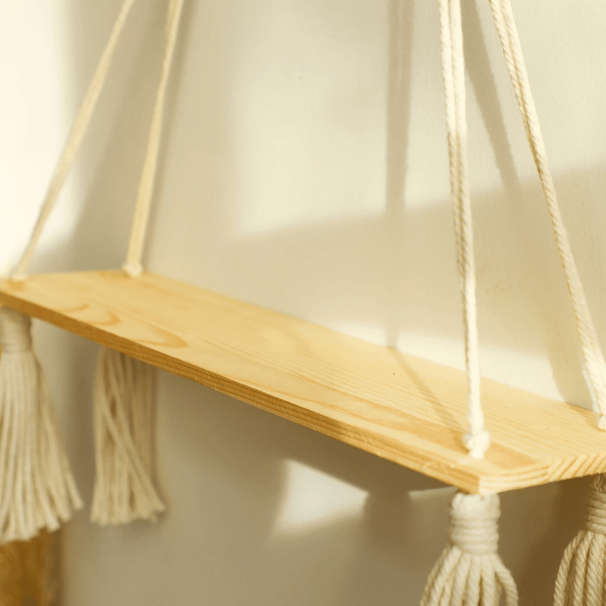 Boho hanging shelf of light wood held by hand knotted white macrame