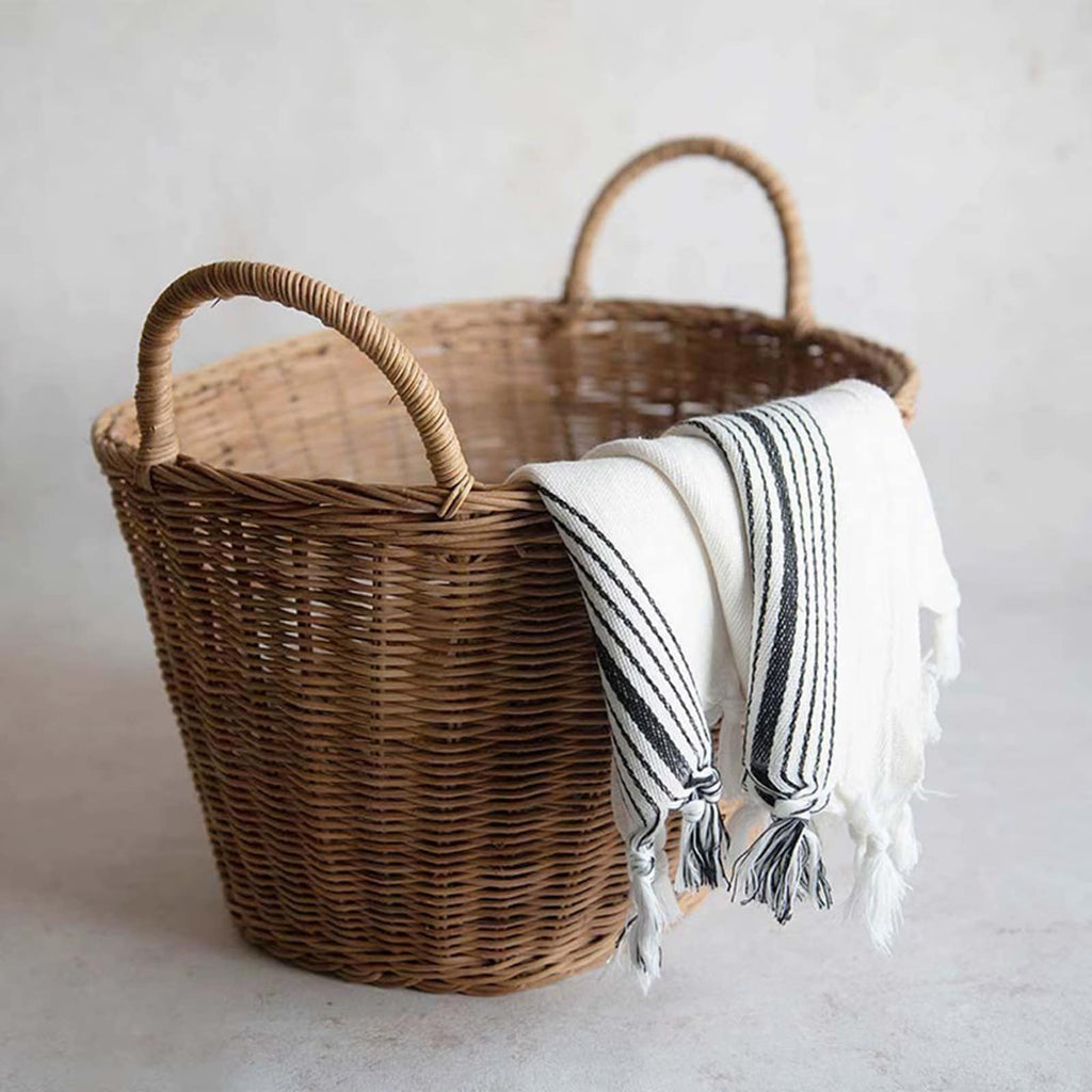 Brown wicker tote basket with two handles holding a throw