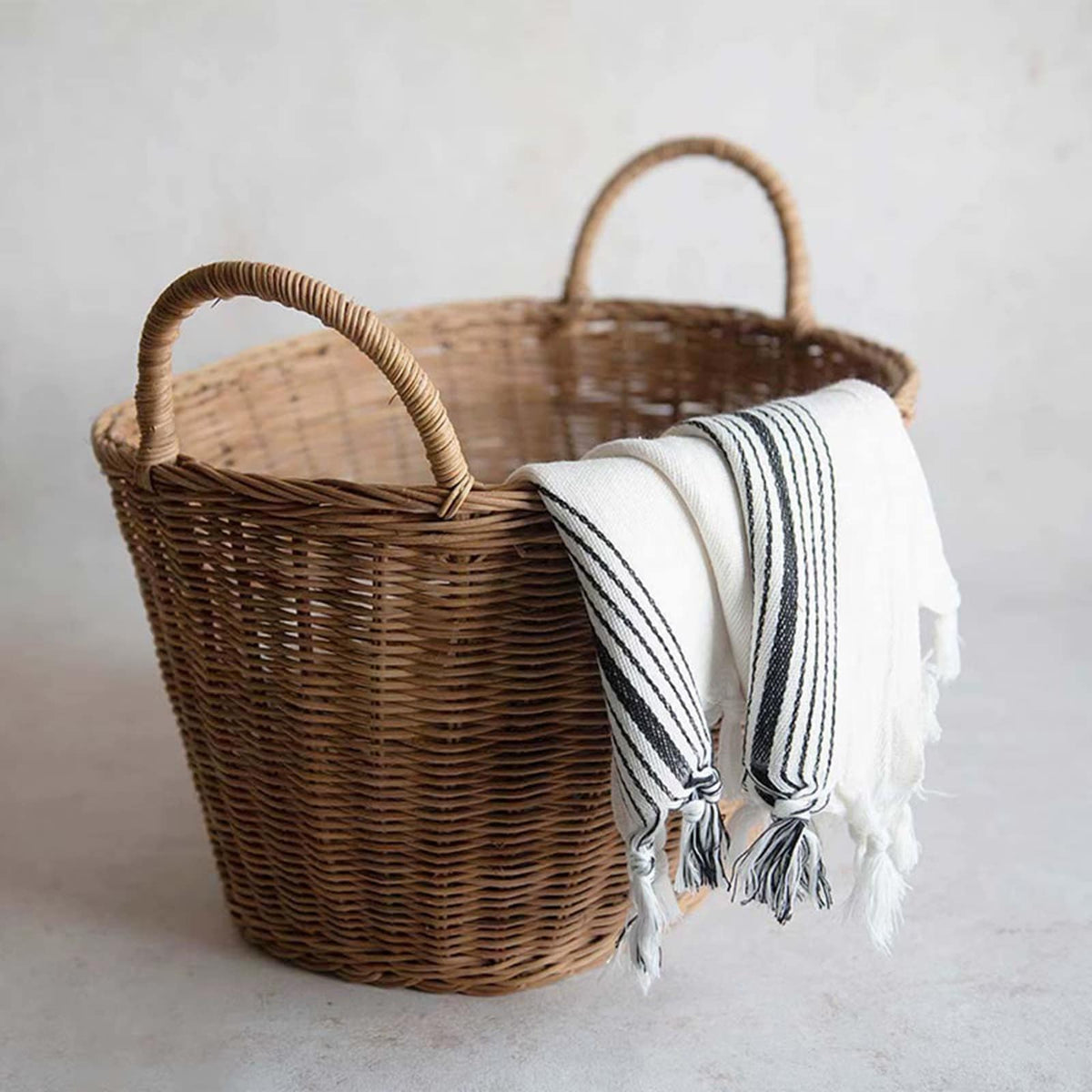 Brown wicker tote basket with two handles holding a throw