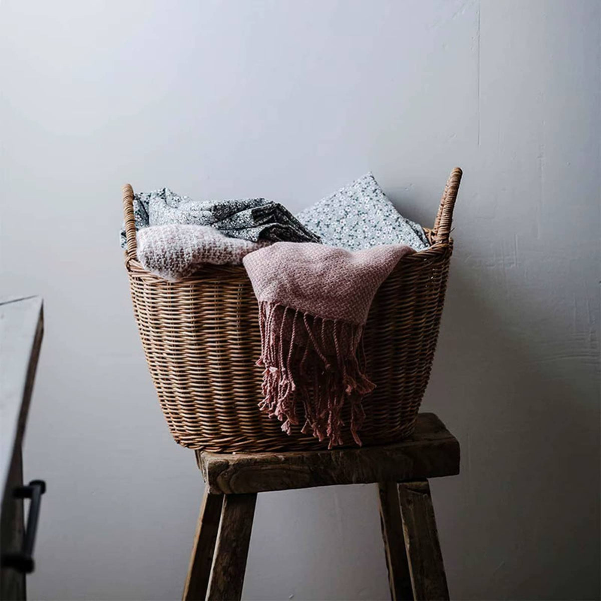 Brown wicker tote basket with two handles holding a throw