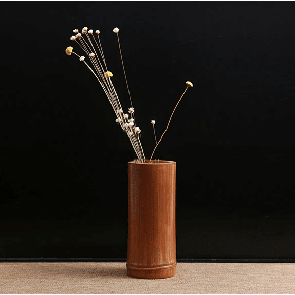 Small dark bamboo tube vase holding dried stems