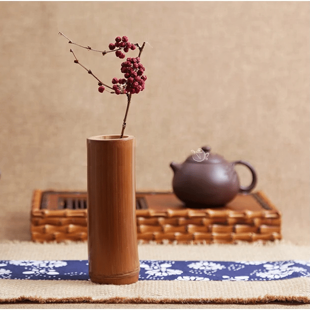 Small dark bamboo tube vase holding dried stems