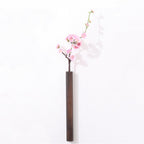 Slim dark wood wall vase holding a single stem