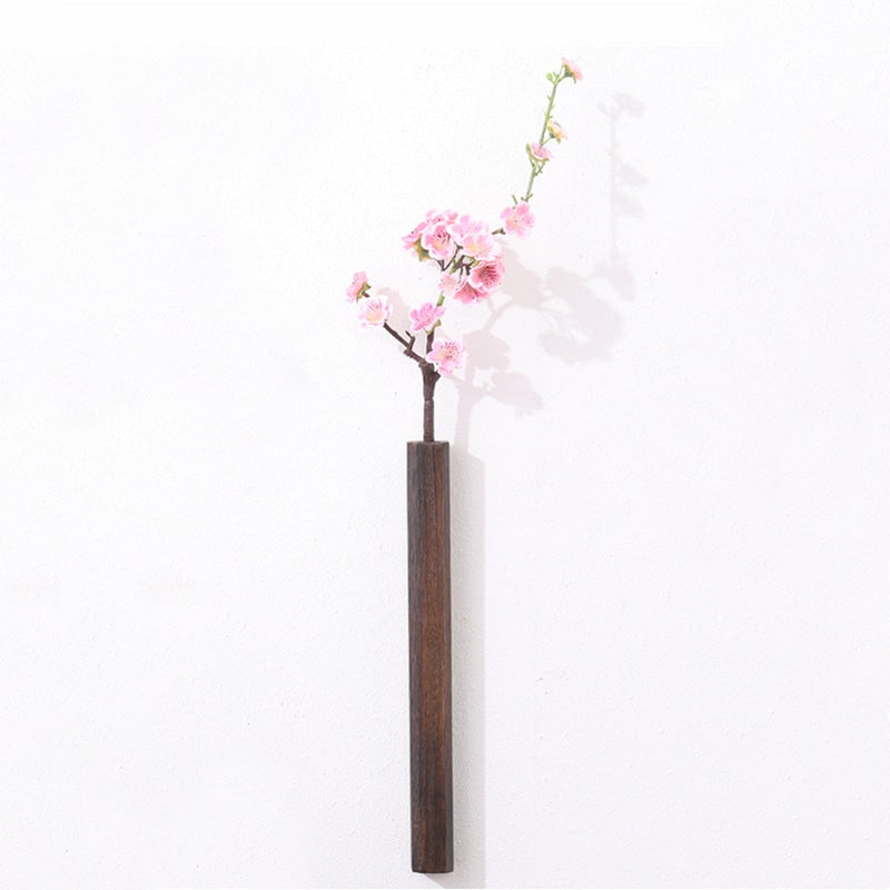 Slim dark wood wall vase holding a single stem