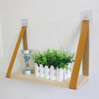 Light wood shelf hanging from two tan faux leather straps