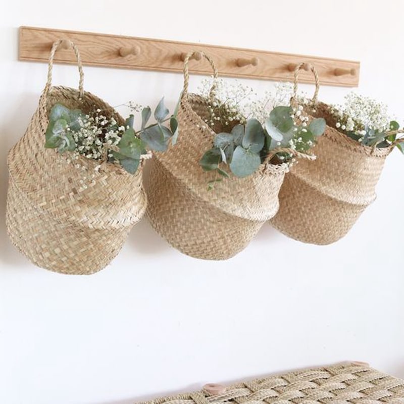 Three small woven belly baskets hanging on wall hooks with plants