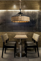 Industrial pendant light with a round black metal frame and a hand woven wicker shade hung by a rope
