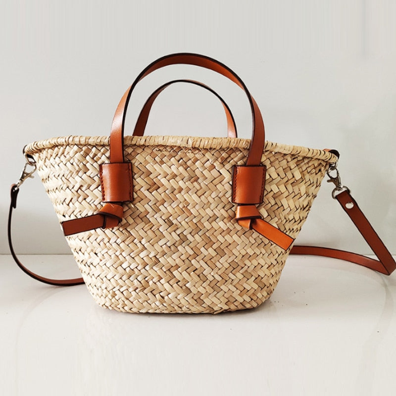 Large brown woven straw handbag with short handles and a camel crossbody strap