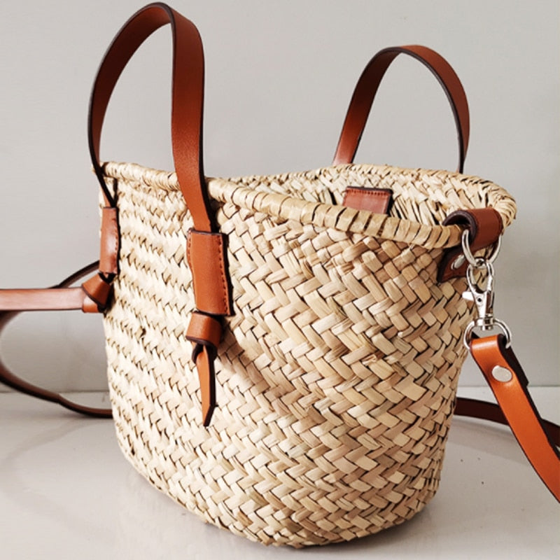 Large brown woven straw handbag with short handles and a camel crossbody strap