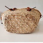 Large brown woven straw handbag with short handles and a camel crossbody strap