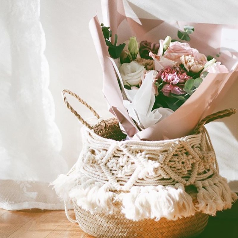 Woven belly basket with macrame sleeve and fringe holding a plant