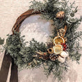 Natural wicker wreath base shown decorated with greenery and dried orange slices