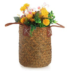 Two tall natural woven baskets with leather handles, one with flowers