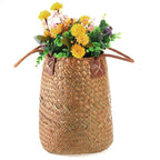 Two tall natural woven baskets with leather handles, one with flowers