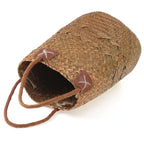 Two tall natural woven baskets with leather handles, one with flowers