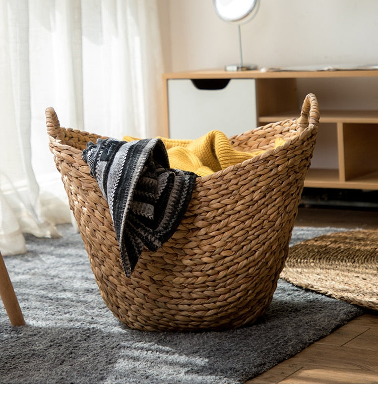 Wide natural woven laundry basket with handles holding throws