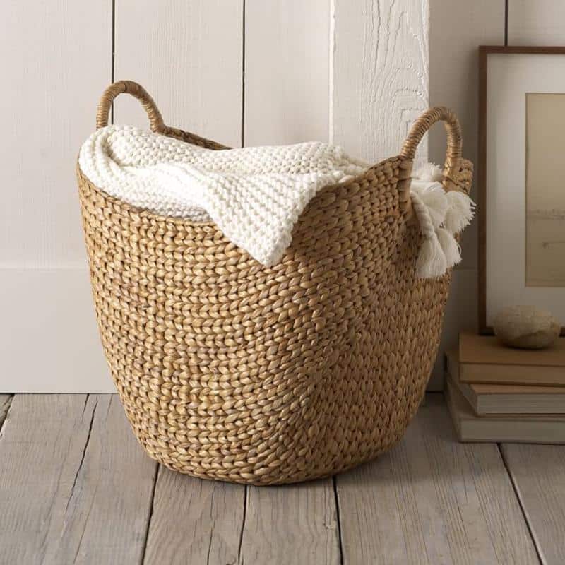 Wide natural woven laundry basket with handles holding throws