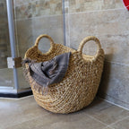 Wide natural woven laundry basket with handles holding throws