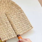 Arched woven paddle hand fan with an orange wrapped handle and loop