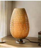 Oval bedside lamp with a hand woven rattan shade on a metal base