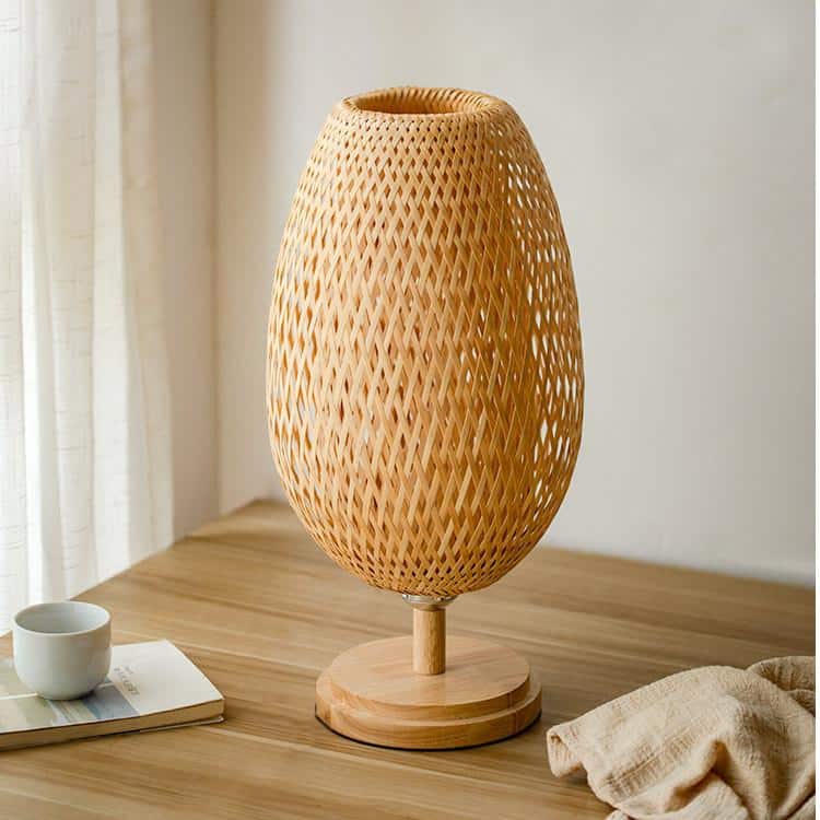 Oval bedside lamp with a hand woven rattan shade on a turned wood base