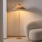 Rattan floor lamp with a wide woven hat shaped shade and a round gold base