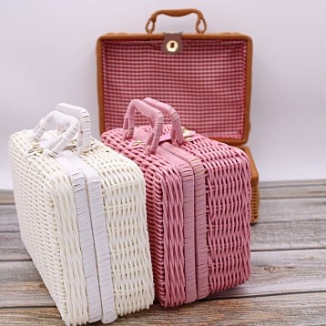 Small pink woven rattan box shaped like a retro suitcase with straps