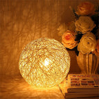 Small rattan ball table lamp glowing on a wooden stand