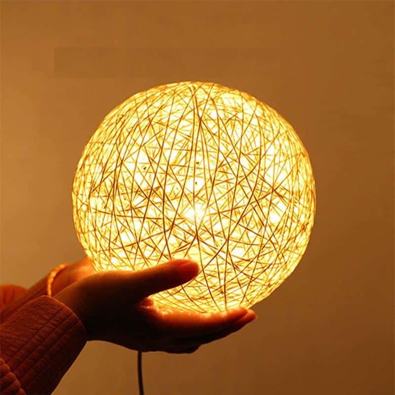 Small rattan ball table lamp glowing on a wooden stand