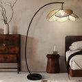 Tall floor lamp with hand woven rattan petals opening in a crown on a black stand