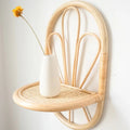 Rattan wall shelf with petal back and cane webbing ledge holding a vase