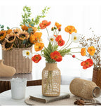 Glass bottle vase wrapped in woven rattan holding poppies