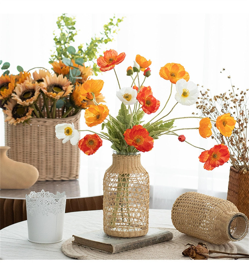 Glass bottle vase wrapped in woven rattan holding poppies