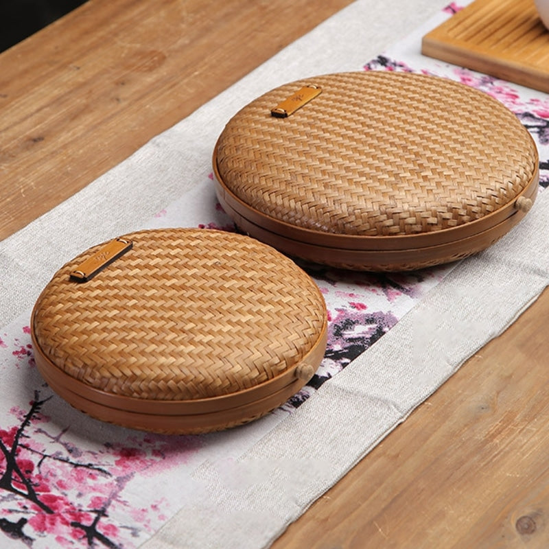Two flat round rattan boxes with fitted lids on a table runner