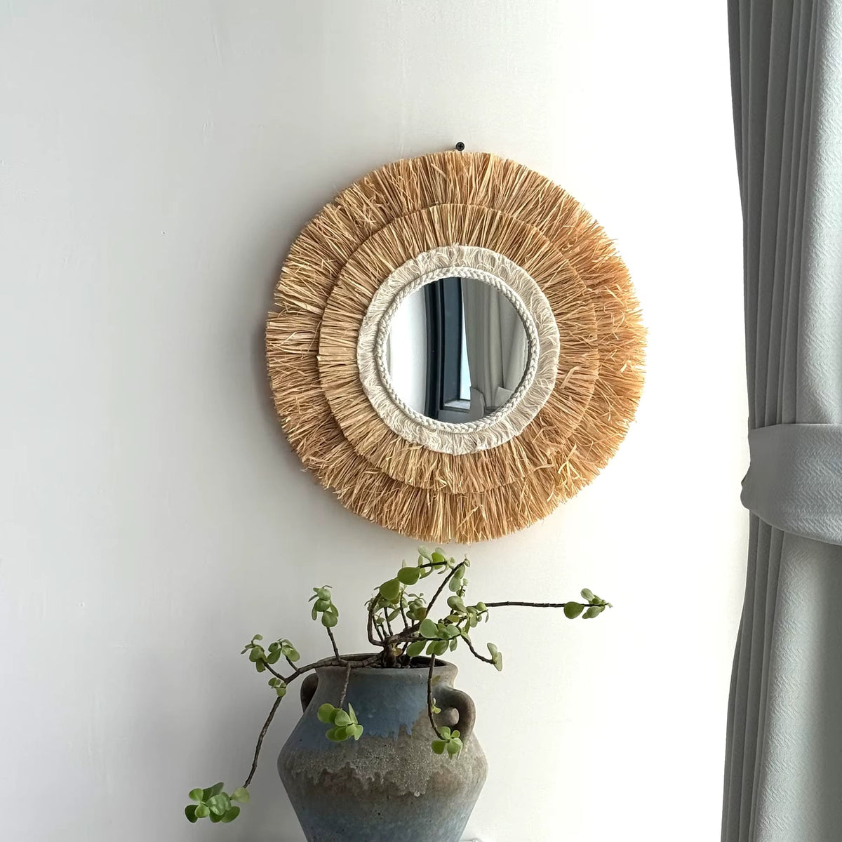 Round mirror framed in layered natural straw fringe