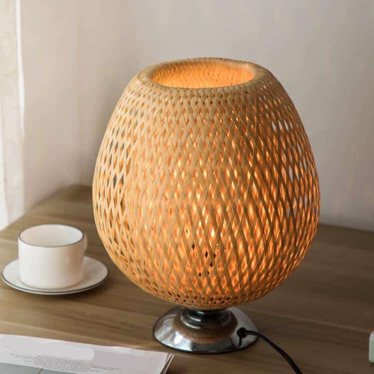 Round bedside lamp with a hand woven rattan shade on a sober metal base