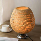 Round bedside lamp with a hand woven rattan shade on a sober metal base