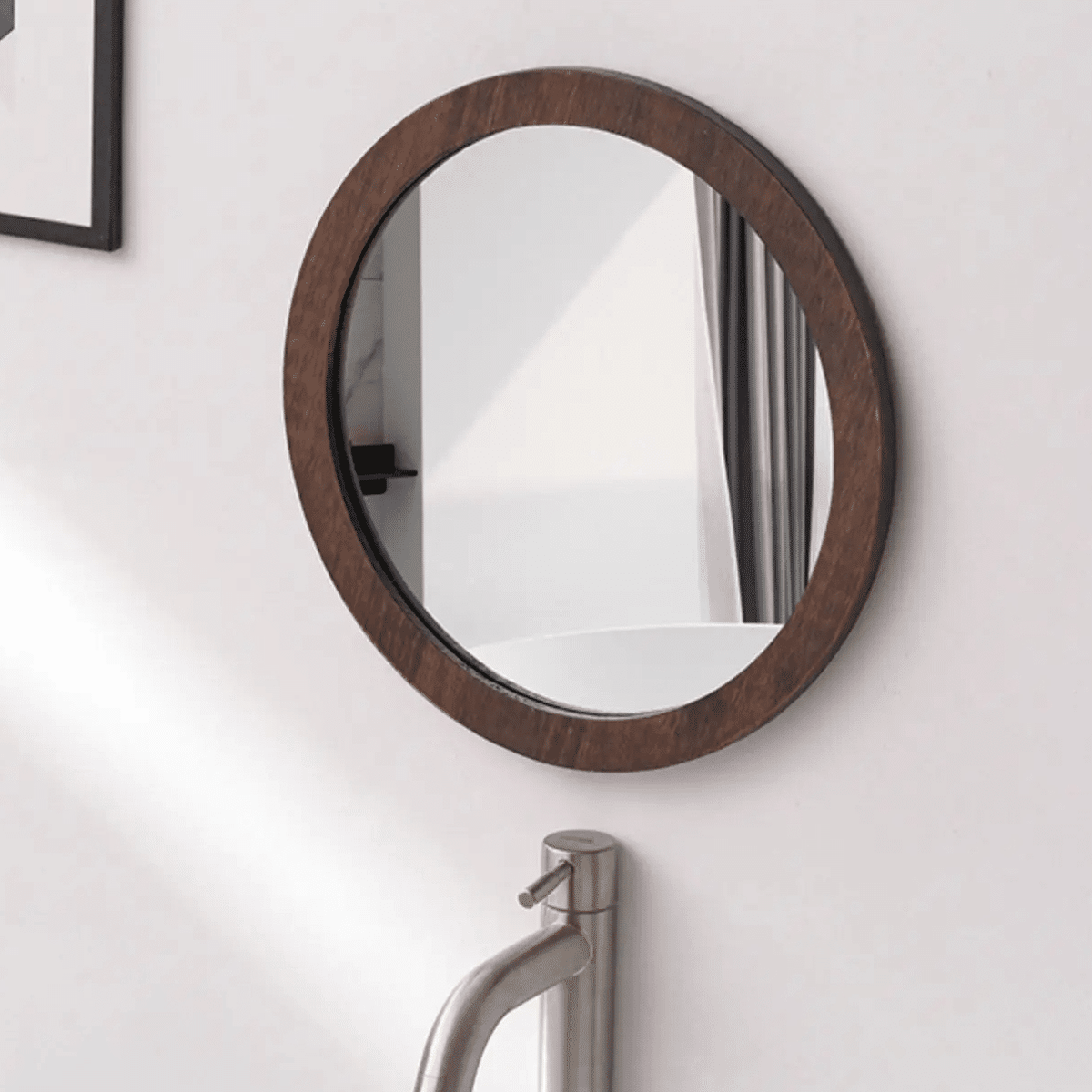 Round wall mirror with a dark wood frame above a sink