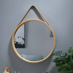 Round light wood mirror hanging from a brown strap