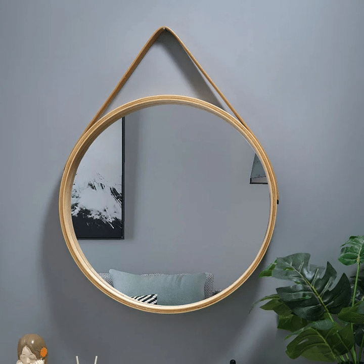 Round light wood mirror hanging from a brown strap