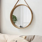 Round light wood mirror hanging from a brown strap