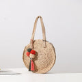 Round hand woven crossbody bag with a textured weave and hand knotted pompoms