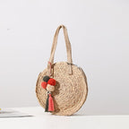 Round hand woven crossbody bag with a textured weave and hand knotted pompoms