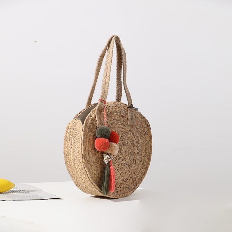 Round hand woven crossbody bag with a textured weave and hand knotted pompoms
