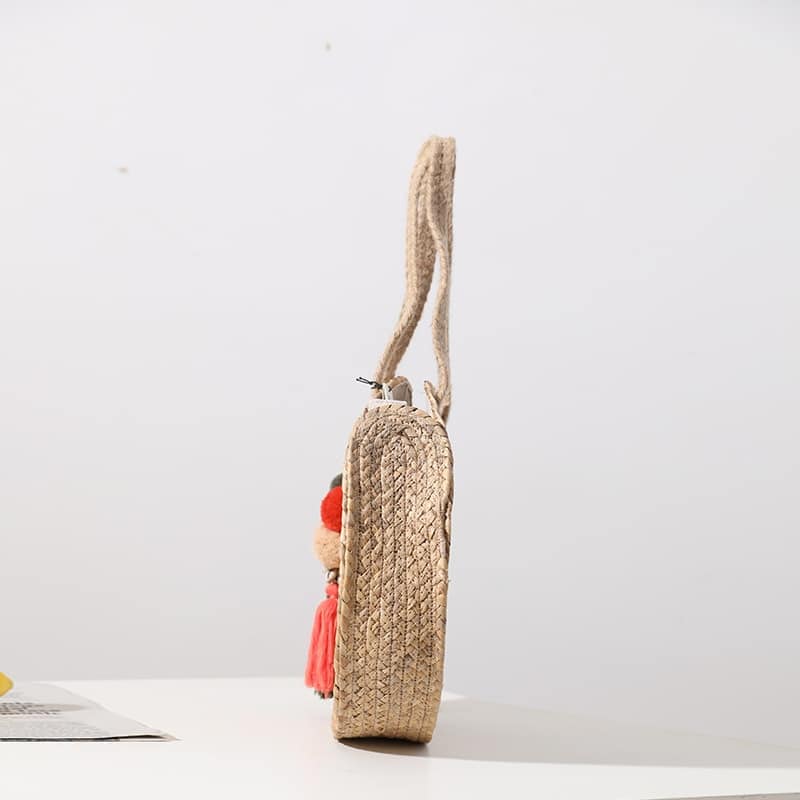 Round hand woven crossbody bag with a textured weave and hand knotted pompoms
