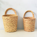 Two natural seagrass wall baskets holding flowers