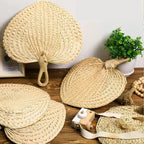 Heart shaped woven hand fans with loop handles set on chairs for a garden wedding
